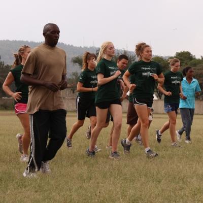 Projects Abroad volunteers get hands-on sports coaching experience in Kenya by leading a warm up Sports enthusiasts jog to warm up during their volunteer sports coaching in Kenya